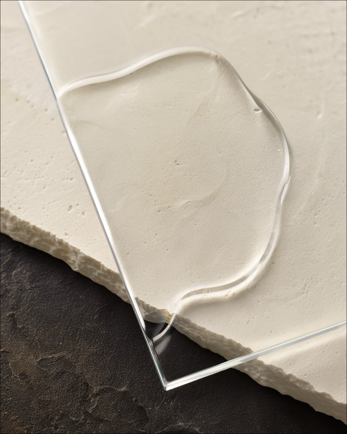 A completely clear oil forms a thin veil across optical glass and ivory limestone.